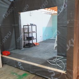 MTS SCHREINER - Wnętrze domu w trakcie budowy: widoczne ściany z izolacją, instalacje elektryczne, regał z narzędziami. Ujęcie z perspektywy wejścia do pomieszczenia.