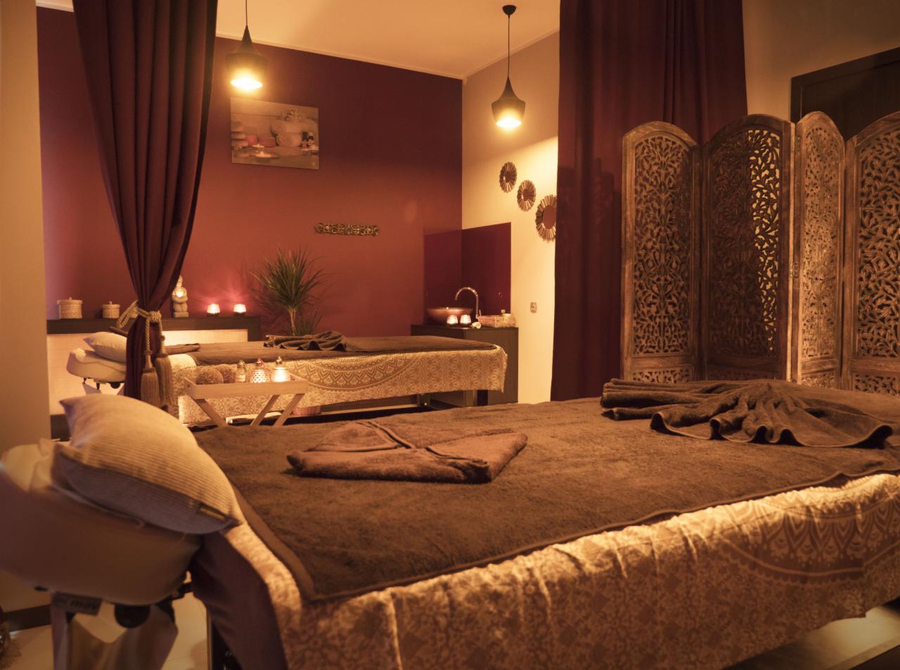 Dwa przygotowane łóżka do masażu w gabinecie SPA z dekoracyjnym parawanem, stonowaną kolorystyką i nastrojowym oświetleniem.