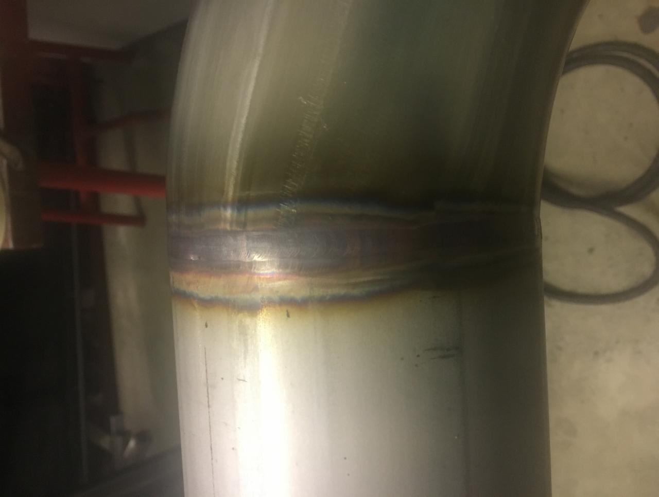 Szczegółowe zbliżenie spoiny na zagiętej, metalowej rurze, widoczne charakterystyczne przebarwienia po spawaniu.