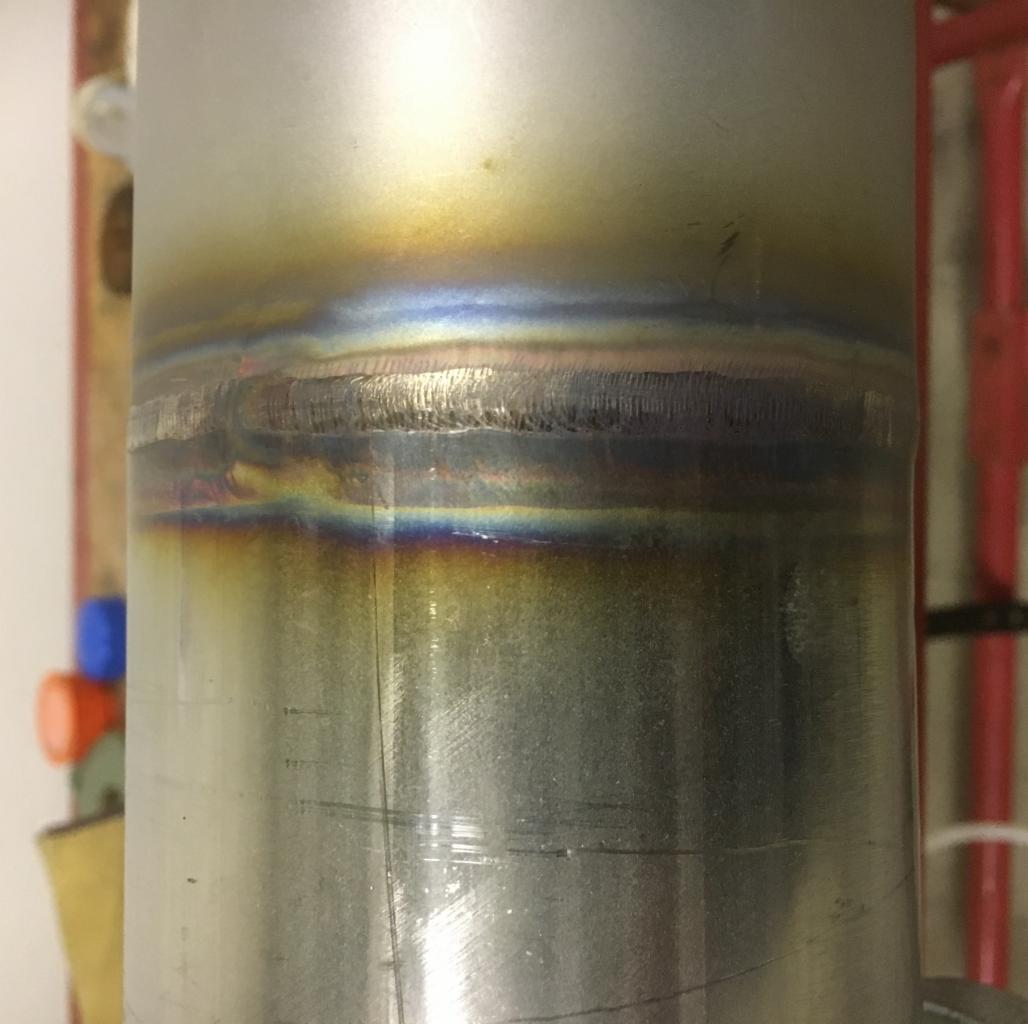 Złącze spawane na rurze ze stali nierdzewnej, widoczne charakterystyczne przebarwienia termiczne w odcieniach tęczy.