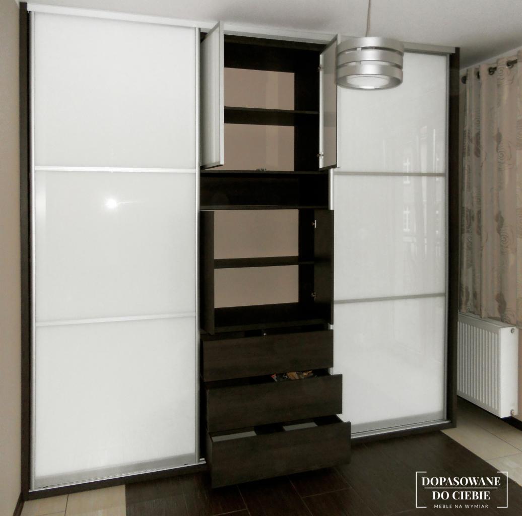 Biało-brązowa szafa przesuwna z otwartymi półkami i szufladami, widoczna część zawartości szuflady na tle parkietu.