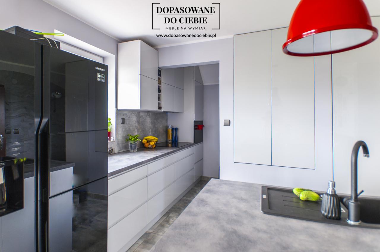 Nowoczesna kuchnia z szarymi frontami i blatem w Gdańsku, z czarną lodówką Samsung i czerwonym elementem oświetleniowym.