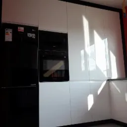 Nowoczesna kuchnia z białymi, błyszczącymi frontami, czarnym obramowaniem i sprzętem AGD: lodówka i piekarnik w zabudowie.