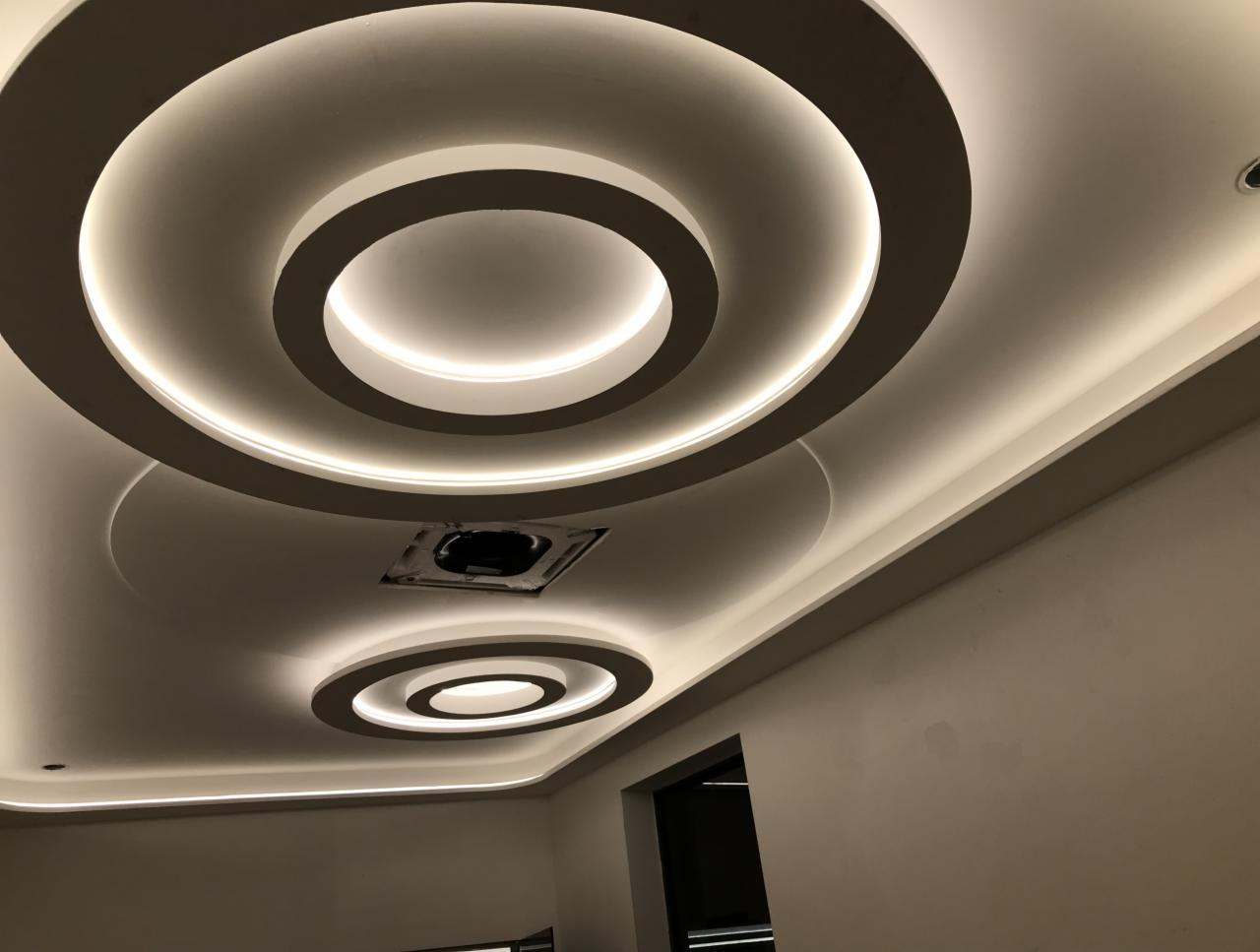 Nowoczesny sufit podwieszany z okrągłymi elementami i podświetleniem LED, widoczne otwory wentylacyjne.