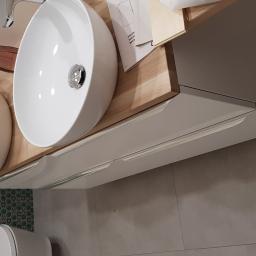 Szymon Zielinski - Dwie białe umywalki nablatowe o zaokrąglonym kształcie z chromowanymi bateriami, zamontowane na drewnianym blacie z szufladami w łazience z zieloną mozaiką na ścianie.