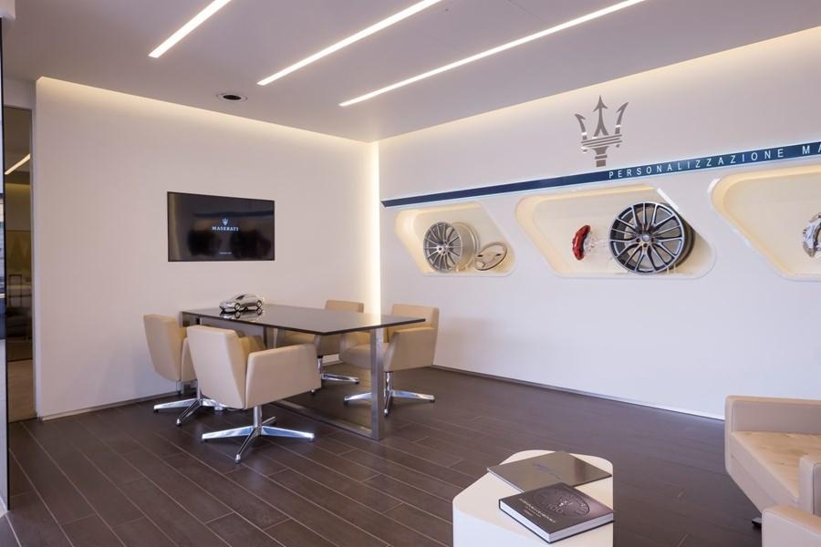 Jasne, nowoczesne wnętrze biura lub salonu z ciemną podłogą, stołem konferencyjnym i ekspozycją felg oraz logo Maserati na ścianie.