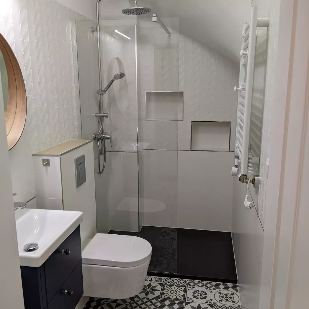 Nowoczesna łazienka na poddaszu z kabiną prysznicową typu walk-in, czarną podłogą w strefie prysznica, białą armaturą i wzorzystymi płytkami podłogowymi.