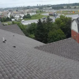 Szary dach pokryty gontem bitumicznym, widok z góry na tle miejskiego krajobrazu w pochmurny dzień.