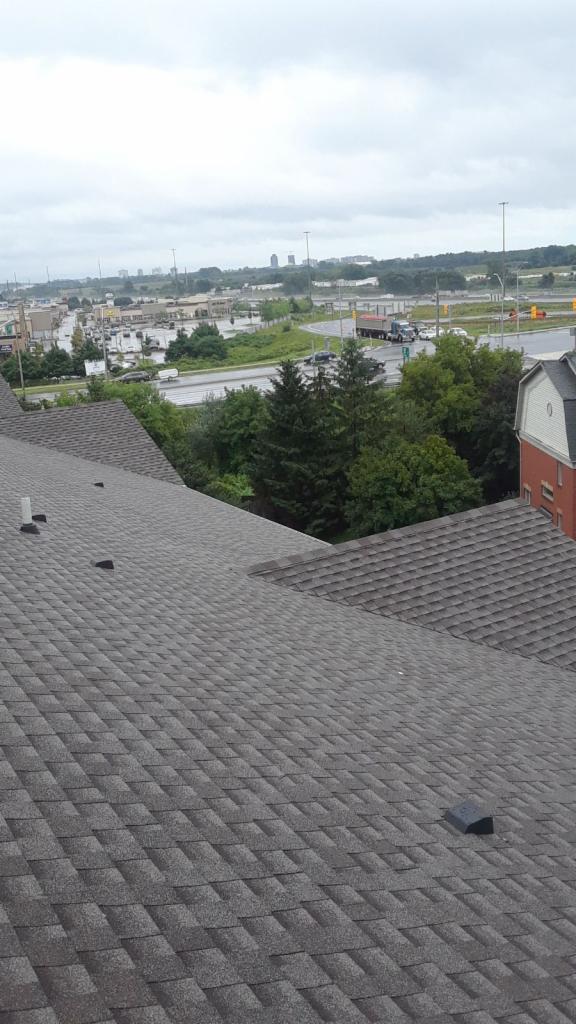 Szary dach pokryty gontem bitumicznym, widok z góry na tle miejskiego krajobrazu w pochmurny dzień.