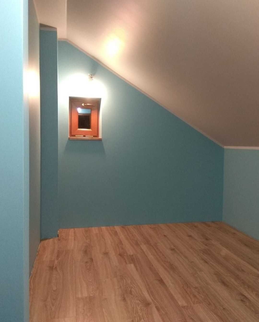 Turkusowe ściany w pokoju na poddaszu z drewnianą podłogą i małym oknem w drewnianej ramie