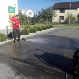 Action Direct Cleaning - Pracownik w czerwonej koszulce czyści kostkę brukową przed sklepem Top Market za pomocą myjki ciśnieniowej, widoczne efekty czyszczenia.