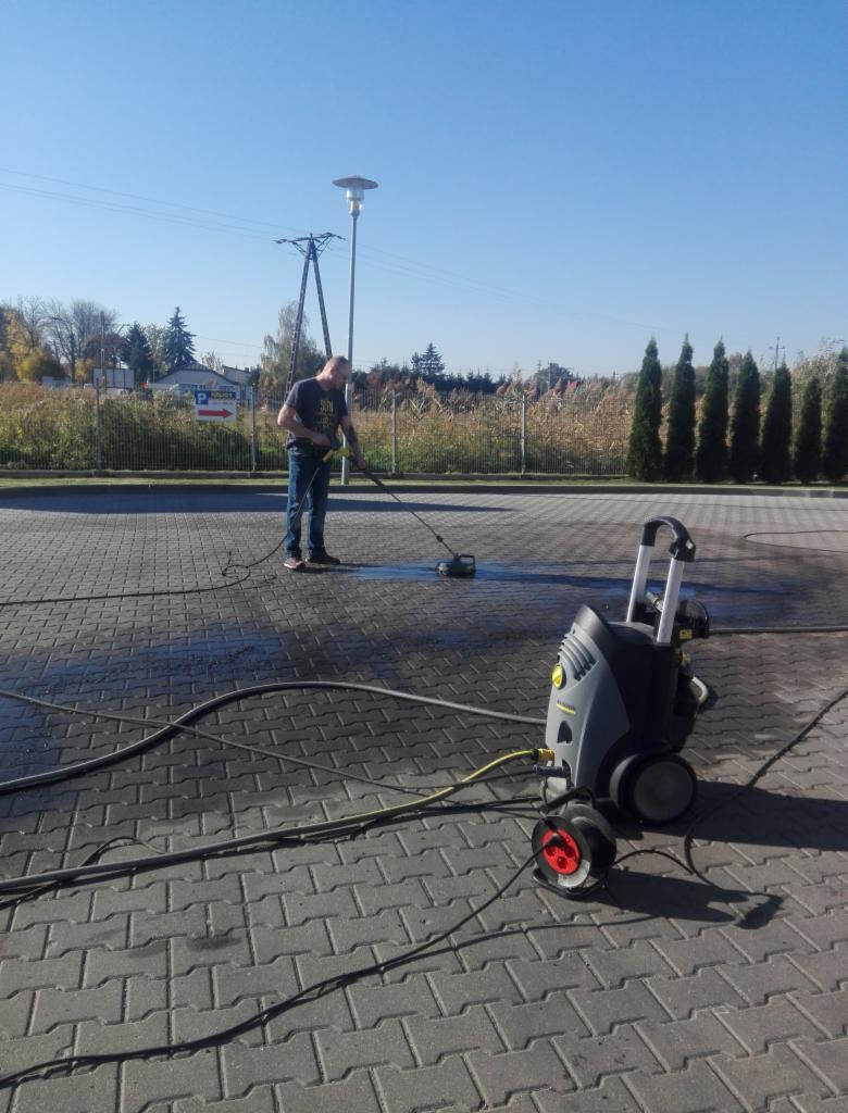 Mężczyzna w trakcie czyszczenia kostki brukowej myjką ciśnieniową Kärcher na zewnątrz, widoczne ślady wilgoci i urządzenie czyszczące.