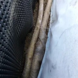 Ułożone rury drenarskie owinięte geowłókniną, otoczone warstwą żwiru i folią kubełkową, zabezpieczone przed gruntem