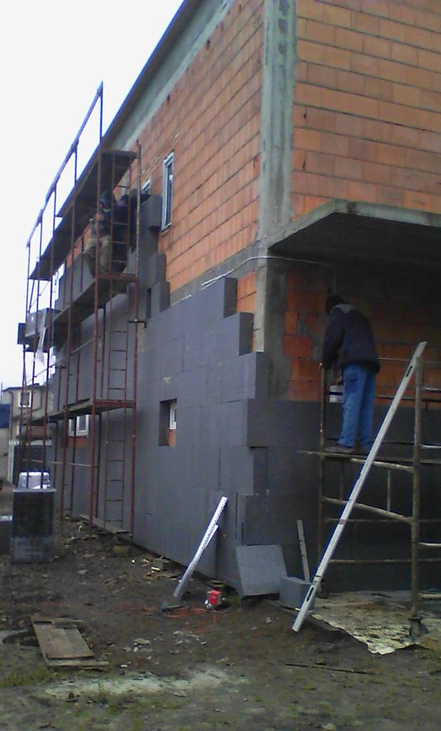 Prace związane z ociepleniem budynku styropianem w Tychach, widoczne rusztowania i pracownicy podczas montażu, ceglana elewacja w tle.