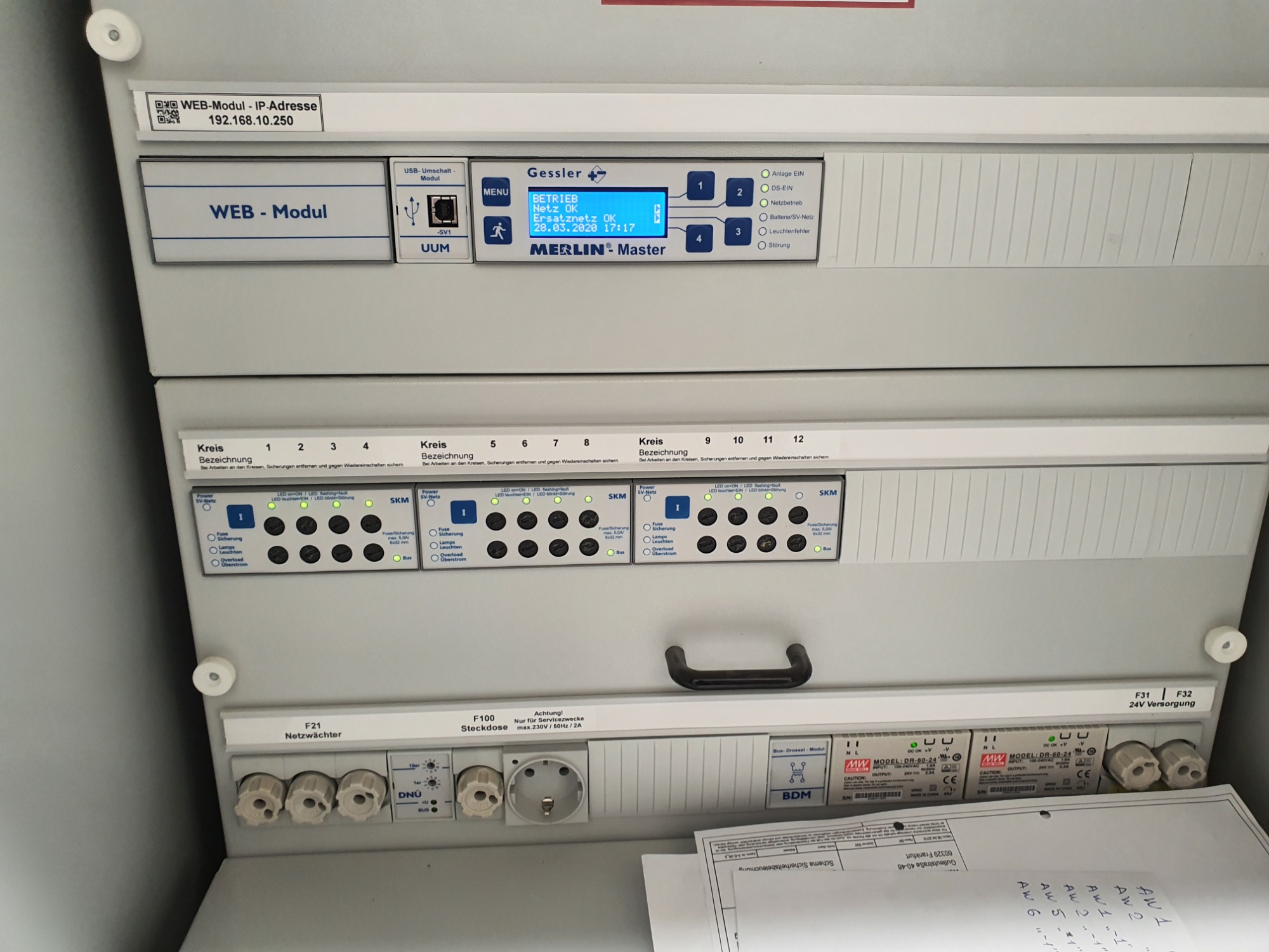 Szczegółowe ujęcie rozdzielni elektrycznej z modułem WEB, wyświetlaczem Gessler Merlin Master pokazującym status sieci i zasilania awaryjnego, bezpiecznikami, gniazdem serwisowym i schematem...