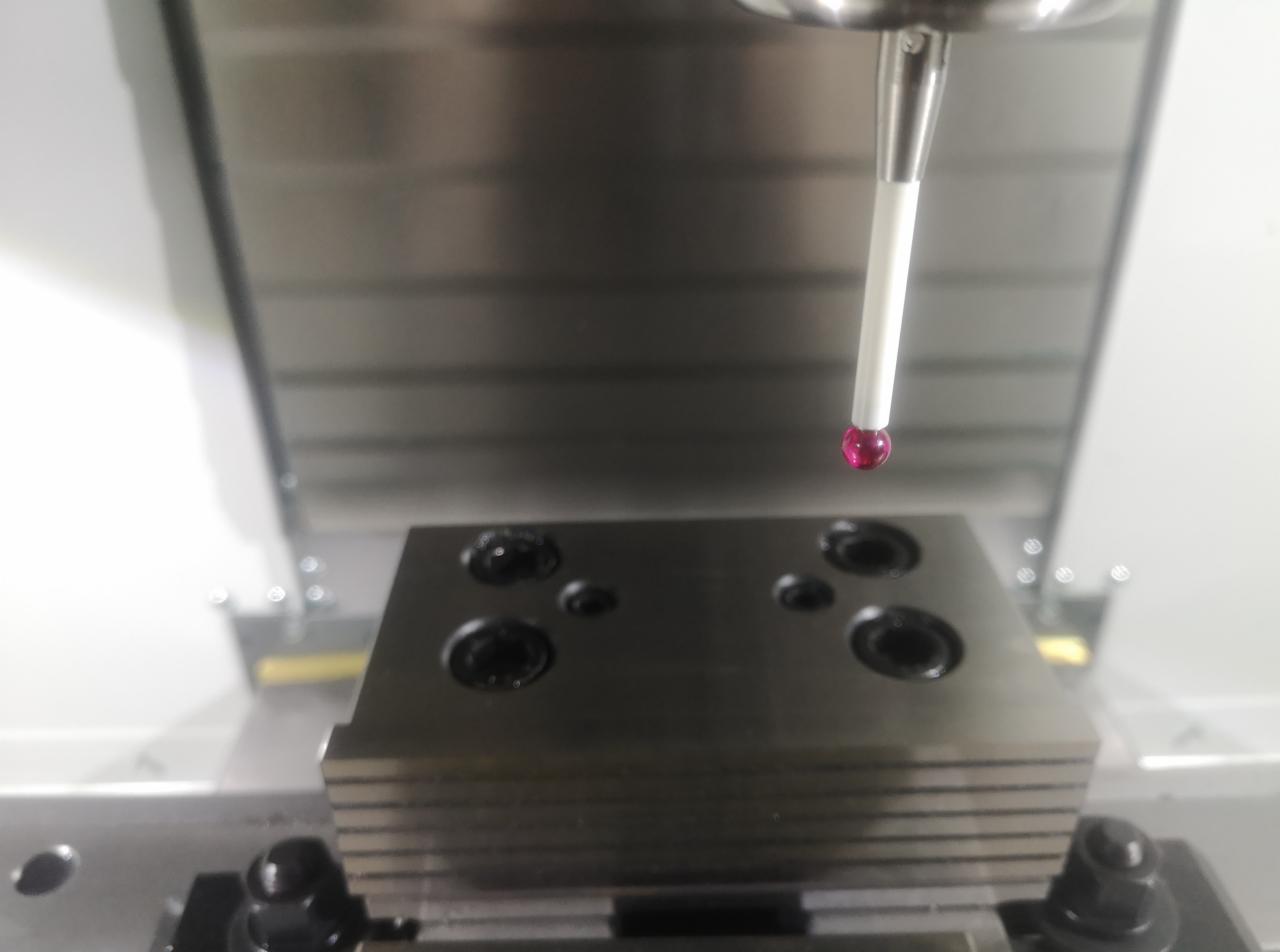 Pomiar detalu na obrabiarce CNC z użyciem sondy pomiarowej z rubinową kulką. Widoczne otwory w obrabianym elemencie.