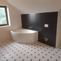 Narożna wanna w łazience z czarnymi płytkami ściennymi i biało-czarną podłogą w karo, widoczne przyłącza wodne i okno dachowe.