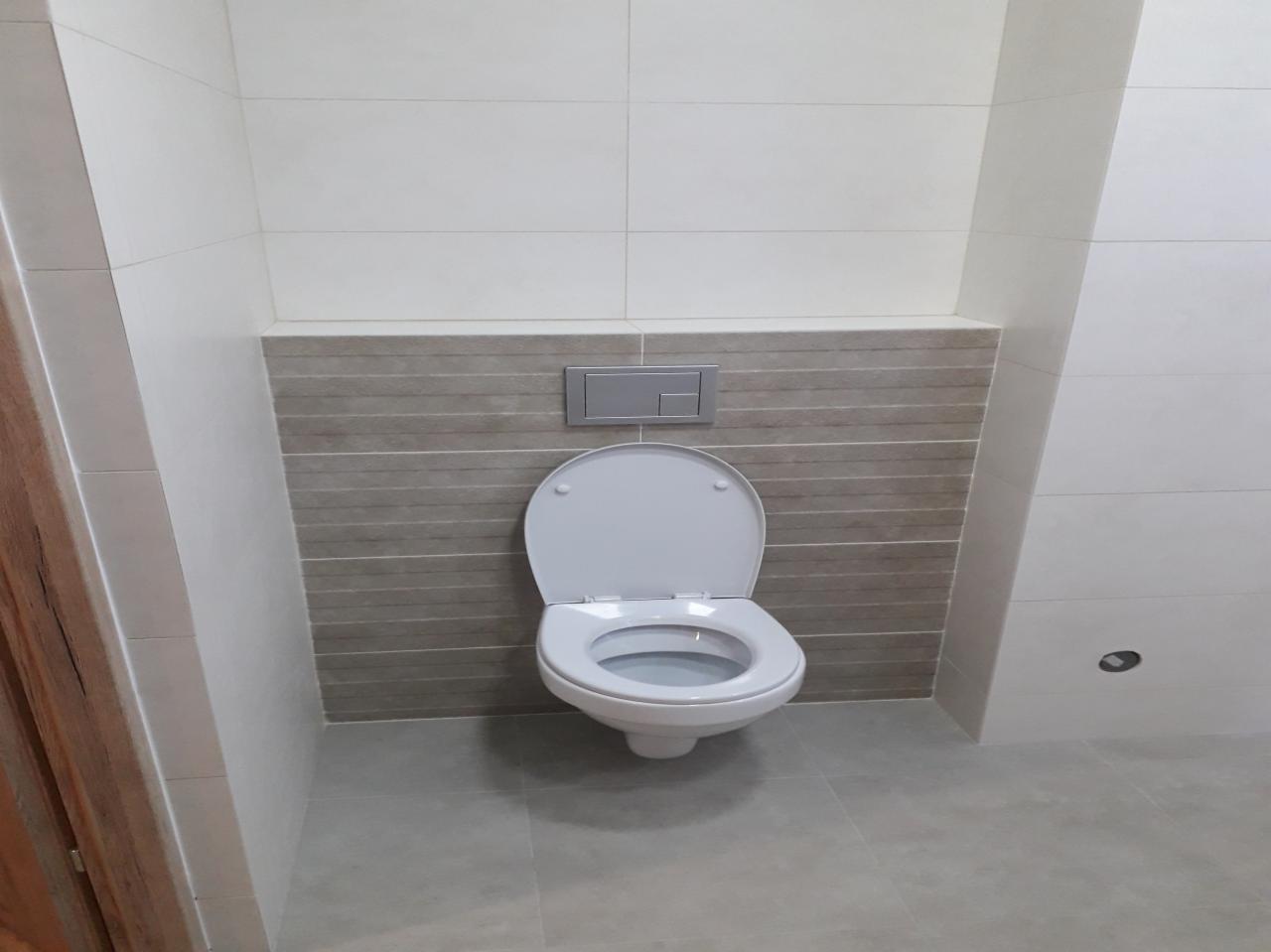 Nowoczesna toaleta podwieszana z szarymi płytkami imitującymi drewno w Bochni, widok z przodu, otwarte siedzisko.