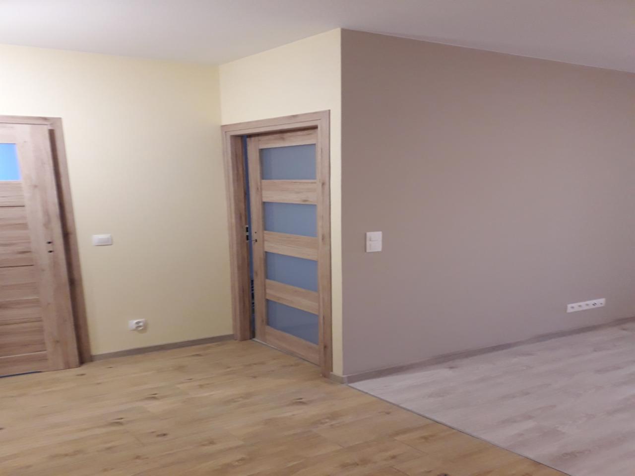 Wnętrze po odświeżeniu: Dwa rodzaje drewnopodobnej podłogi, ściany pomalowane na dwa kolory - beżowy i jasnobrązowy, dwoje drewnianych drzwi z przeszkleniami.