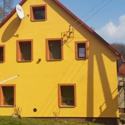 POL BAU STOKLOSA SPÓŁKA Z OGRANICZONĄ ODPOWIEDZIALNOŚCIĄ - Żółta elewacja domu jednorodzinnego z brązowymi obramowaniami okien, widoczna antena satelitarna i rozkładana suszarka na pranie, częściowo zacieniona fasada.