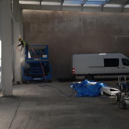 POL BAU STOKLOSA SPÓŁKA Z OGRANICZONĄ ODPOWIEDZIALNOŚCIĄ - Pracownik na podnośniku maluje natryskowo metalową konstrukcję hali w Starych Bogaczowicach, widoczny biały van i sprzęt malarski.