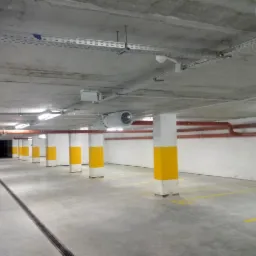 Instalacje elektryczne w garażu podziemnym budynku wielorodzinnego: widoczne koryta kablowe pod sufitem, oświetlenie LED, wentylacja i pomalowane na żółto filary.