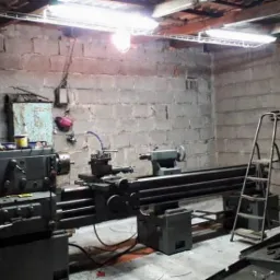 Stary tokarka w warsztacie z surowymi ścianami z pustaków, drabina oparta o ścianę, skrzynka z narzędziami na podłodze