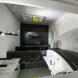 Nowoczesna łazienka z czarno-białymi marmurkowymi płytkami, podwieszaną toaletą, czarnym oświetleniem punktowym i wolnostojącą wanną z czarnymi elementami.