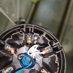 Wnętrze puszki elektrycznej z podłączonymi przewodami: niebieski, czarny, brązowy i biały, z widocznymi śrubami mocującymi.