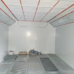 Pusta komora lakiernicza z kratownicą podłogową, oświetleniem sufitowym i instalacją elektryczną w kolorze pomarańczowym.