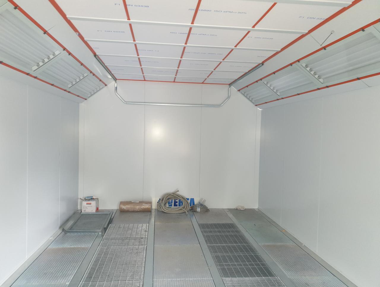 Pusta komora lakiernicza z kratownicą podłogową, oświetleniem sufitowym i instalacją elektryczną w kolorze pomarańczowym.