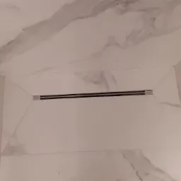 Płytki imitujące marmur na ścianach i suficie łazienki z zamontowanym liniowym odpływem prysznicowym marki Viega.