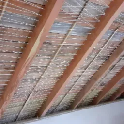 Wnętrze poddasza z widoczną drewnianą konstrukcją dachu i rozciągniętymi białymi linkami, prawdopodobnie przygotowanie do montażu izolacji.