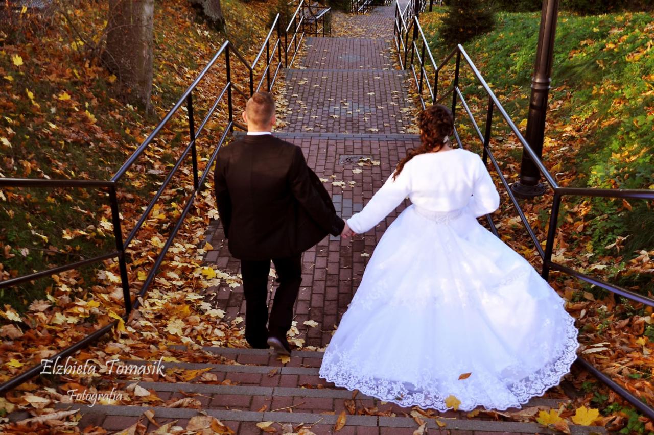 Para młoda trzymająca się za ręce schodzi po schodach z cegły, otoczonych jesiennymi liśćmi i metalowymi barierkami.