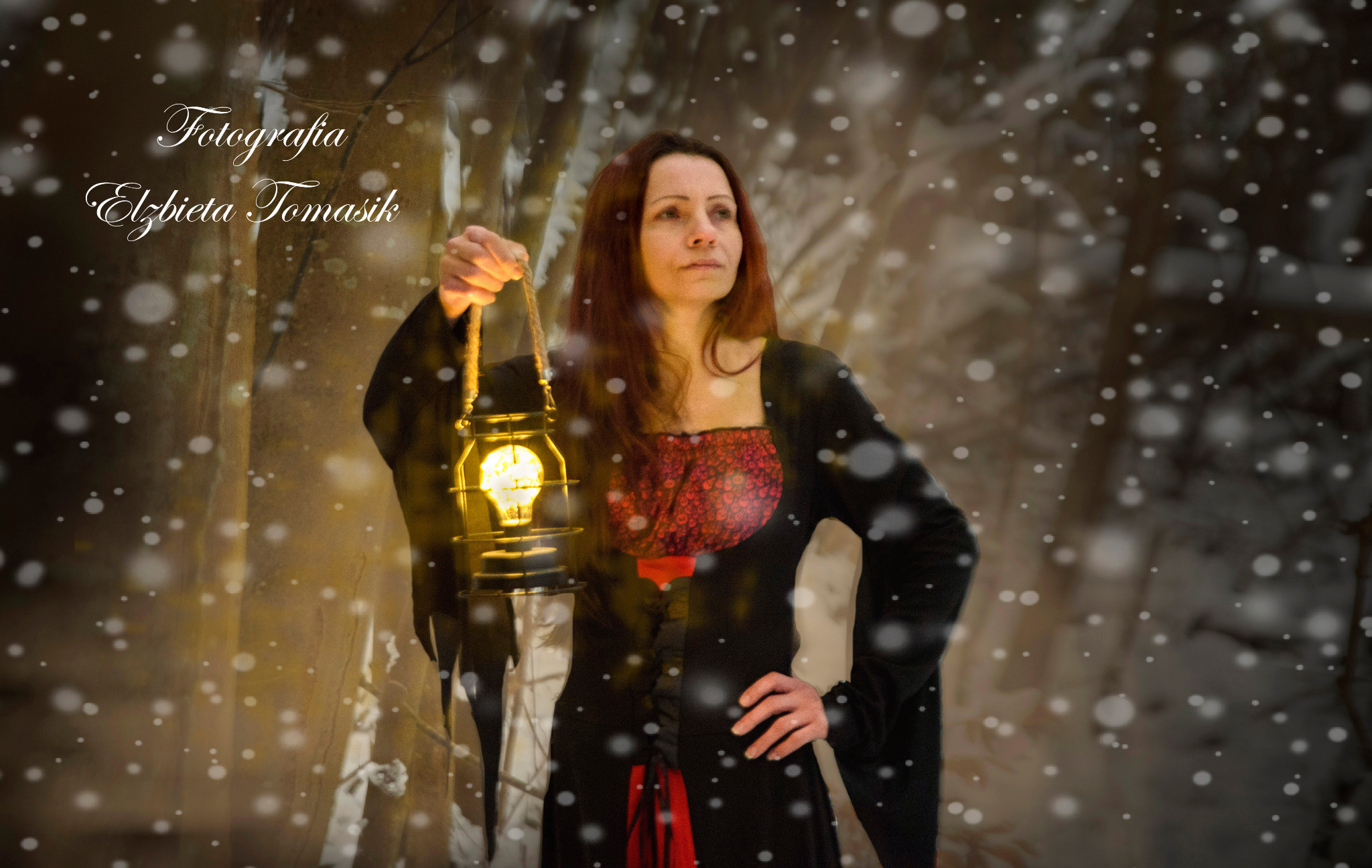 Kobieta z rudymi włosami trzymająca zapaloną latarnię na tle zimowego krajobrazu z padającym śniegiem, ubrana w czarną sukienkę z czerwonymi akcentami.