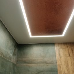 Voytex , Sufity Napinane , Wykonczenia , remonty - Nowoczesny sufit z podświetleniem LED w kształcie prostokąta, brązowa faktura sufitu, ściany wykończone płytkami w odcieniach zieleni i drewnopodobnymi panelami.