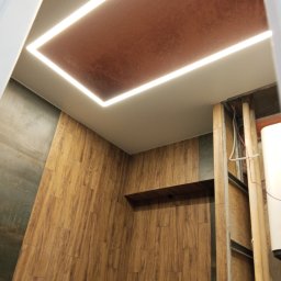 Voytex , Sufity Napinane , Wykonczenia , remonty - Nowoczesny sufit napinany z oświetleniem LED w łazience w Chamsku. Brązowa powierzchnia sufitu i drewnopodobne płytki na ścianach tworzą ciepły klimat.