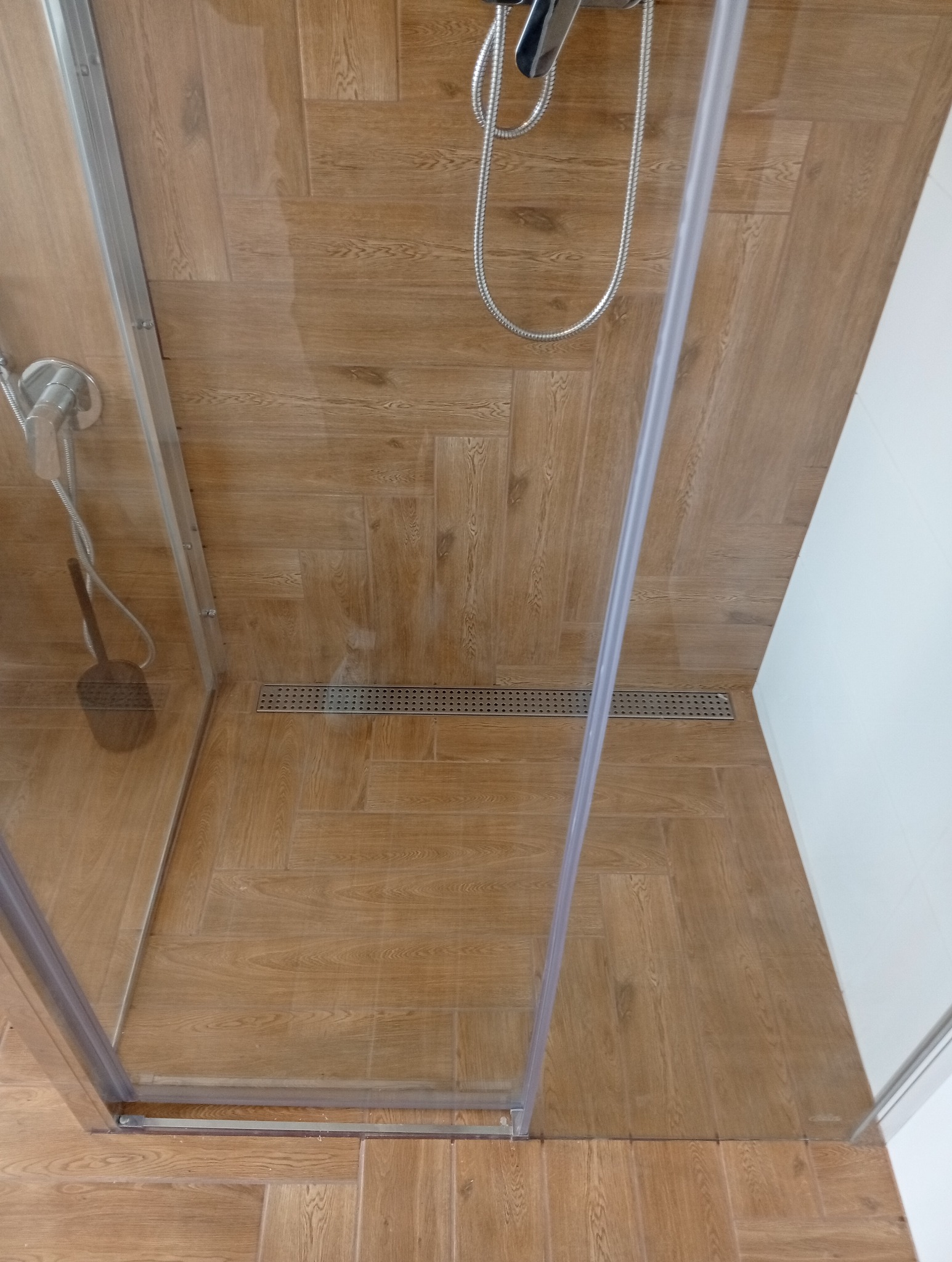 Kabina prysznicowa walk-in z odpływem liniowym i panelami imitującymi drewno, widok z góry, nowoczesne wykończenie łazienki.