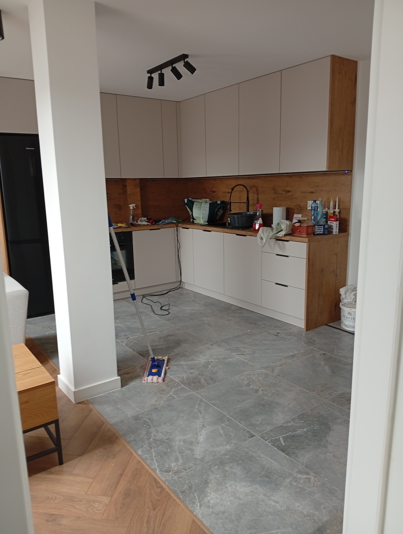 Wykończona kuchnia w Chamsku z szarymi płytkami i białymi szafkami. Widoczny mop sugeruje świeże sprzątanie po remoncie.