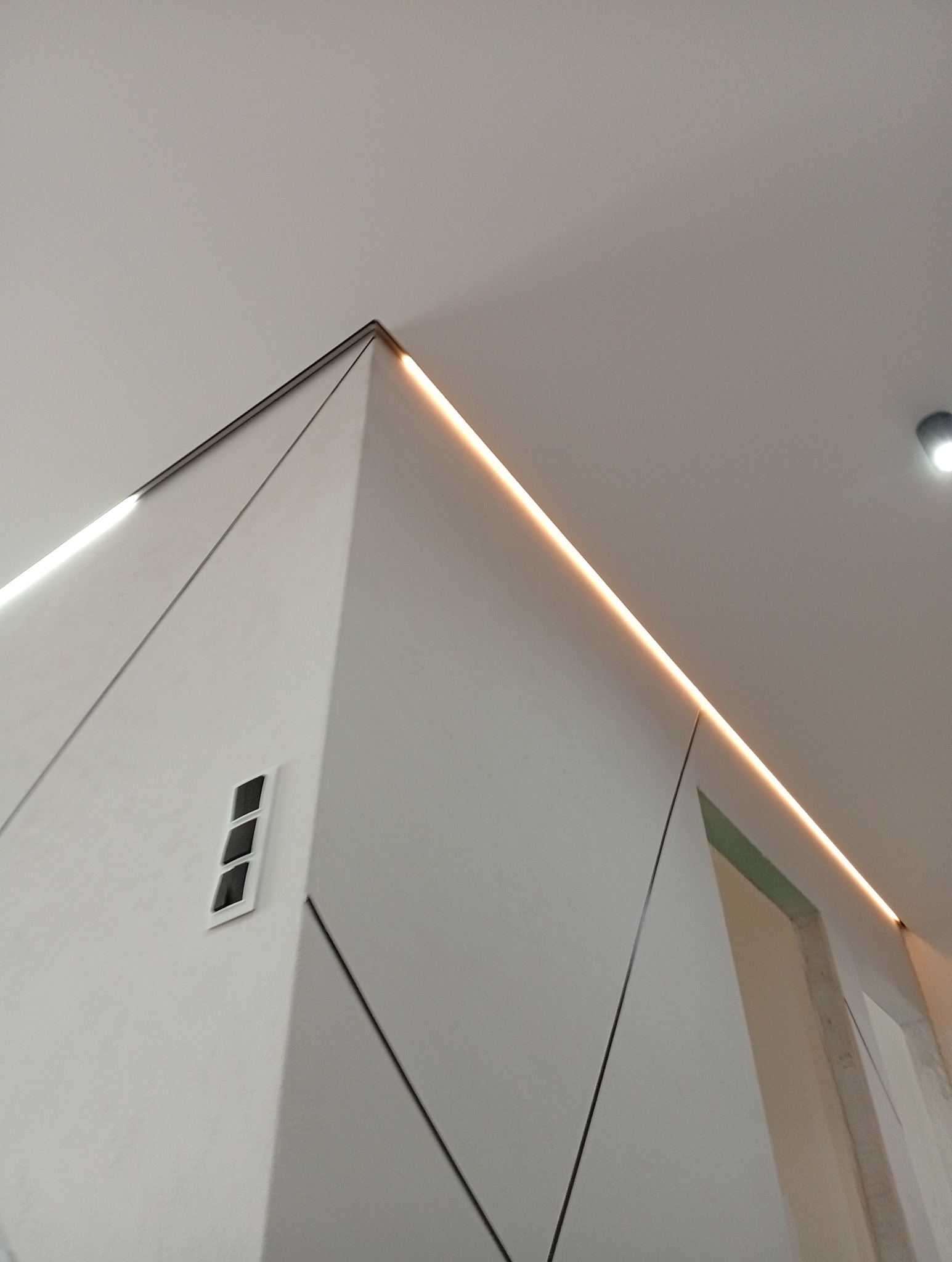 Nowoczesny sufit podwieszany z oświetleniem LED, widok z dołu, geometryczny wzór na ścianie, minimalistyczny design,