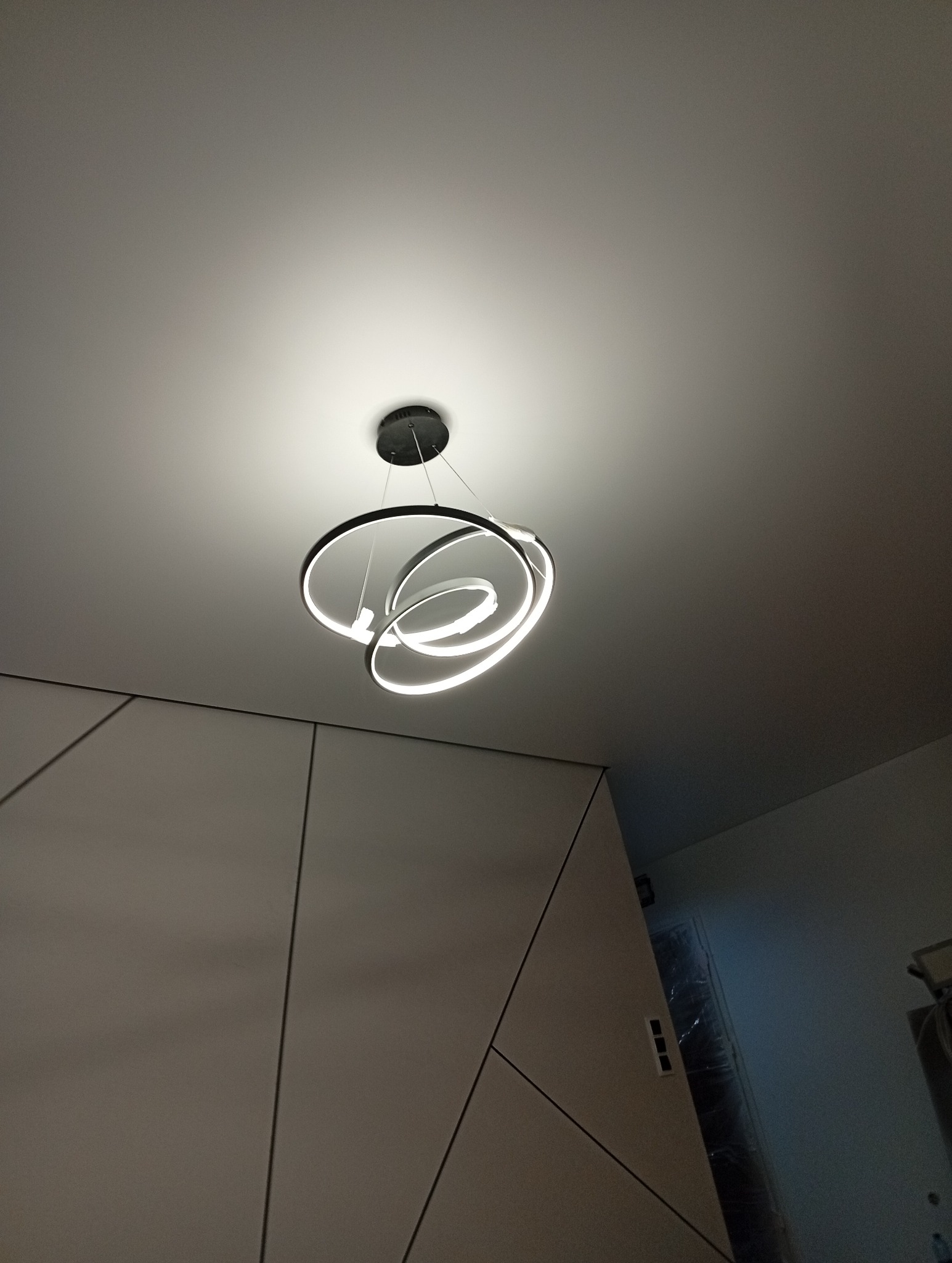 Nowoczesna lampa sufitowa LED z trzema okręgami, tworząca spiralny wzór, zawieszona na białym suficie w minimalistycznym wnętrzu.