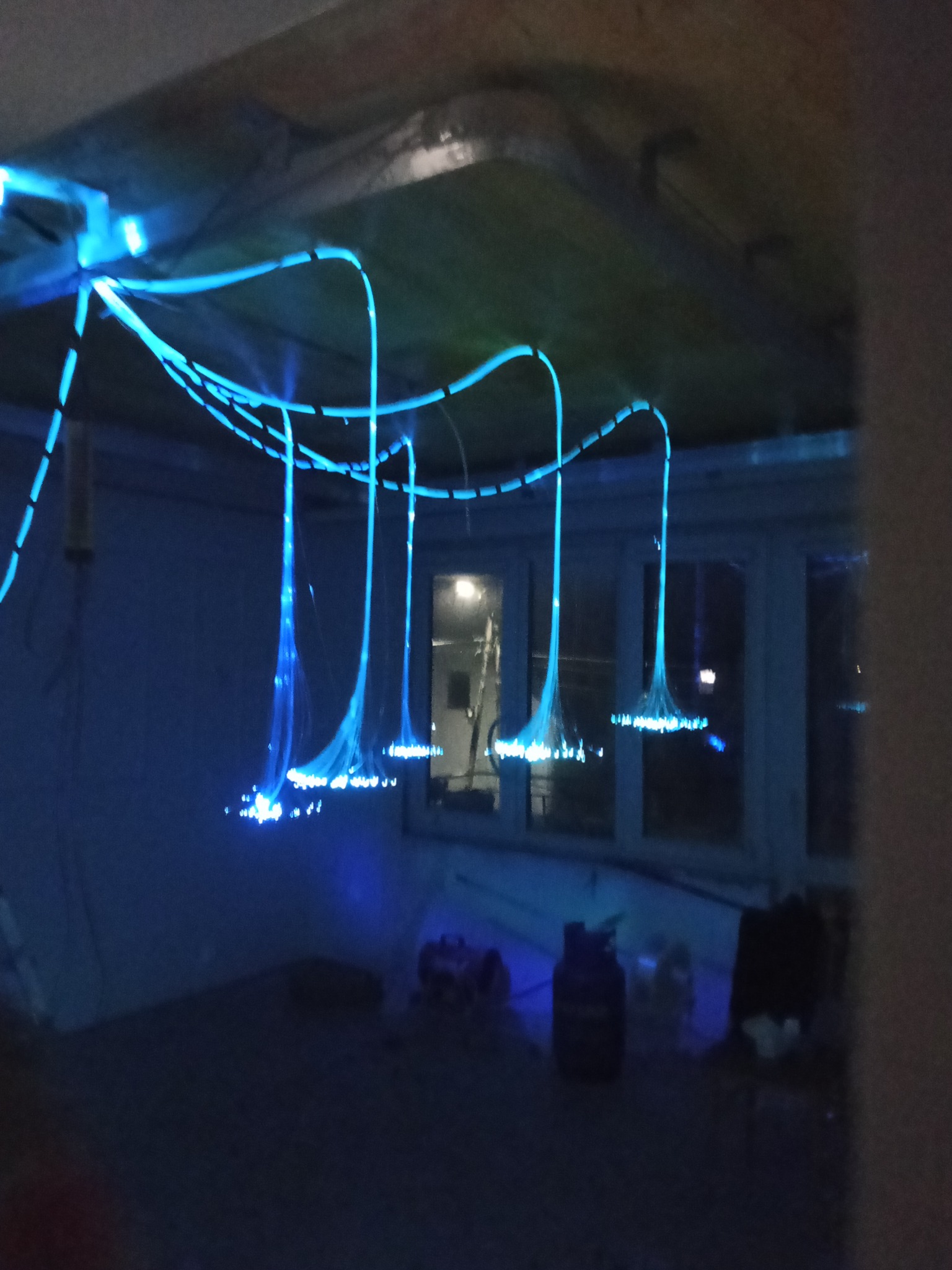 Nastrojowe oświetlenie światłowodowe na suficie, z niebieskimi kablami i punktami świetlnymi, tworzące nowoczesny design wnętrza. Widok z dołu, ciemne otoczenie.