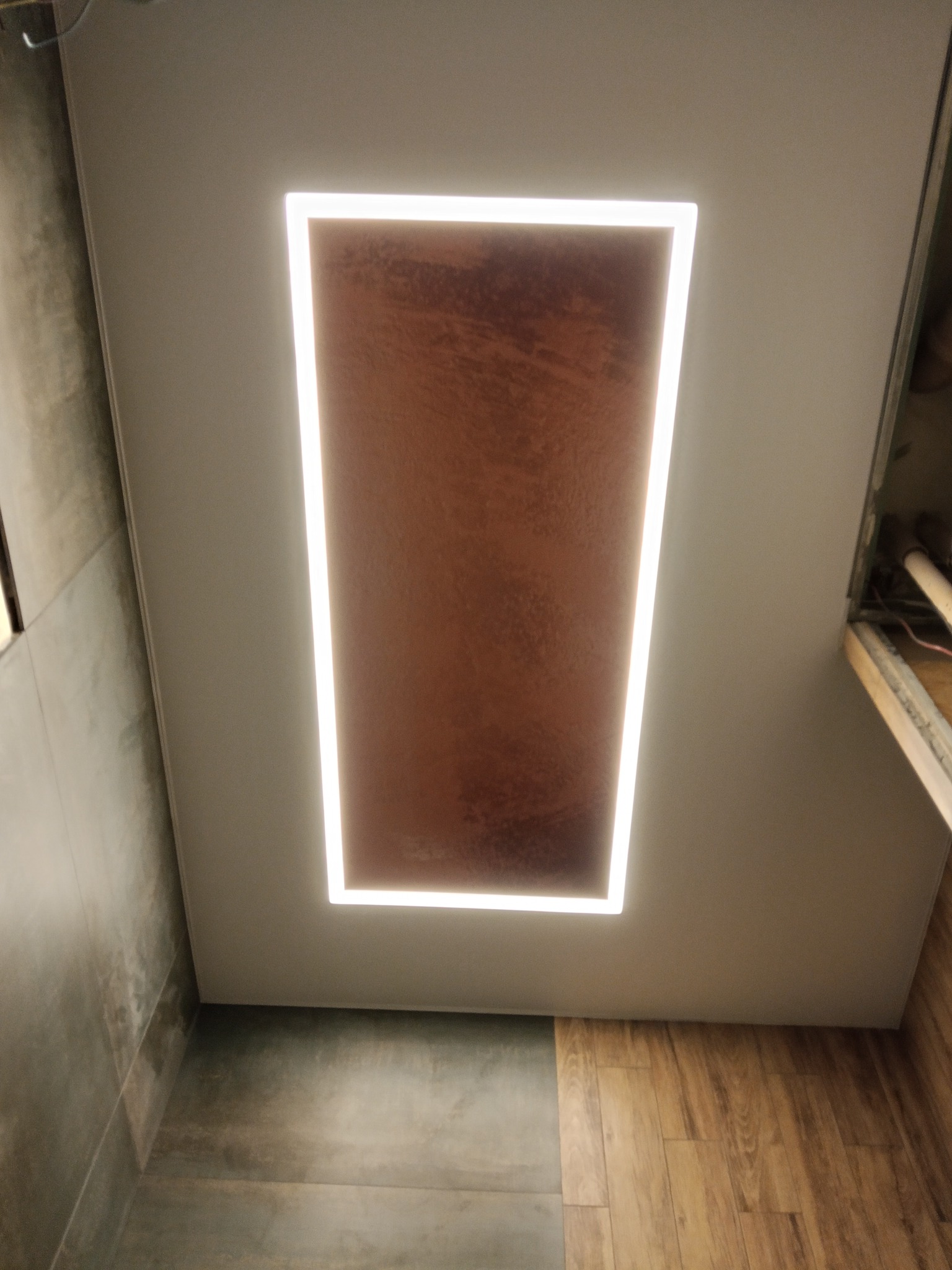 Nowoczesny sufit z podświetlanym panelem w kształcie prostokąta, imitującym miedzianą teksturę. Widoczne płytki podłogowe i fragment ściany.