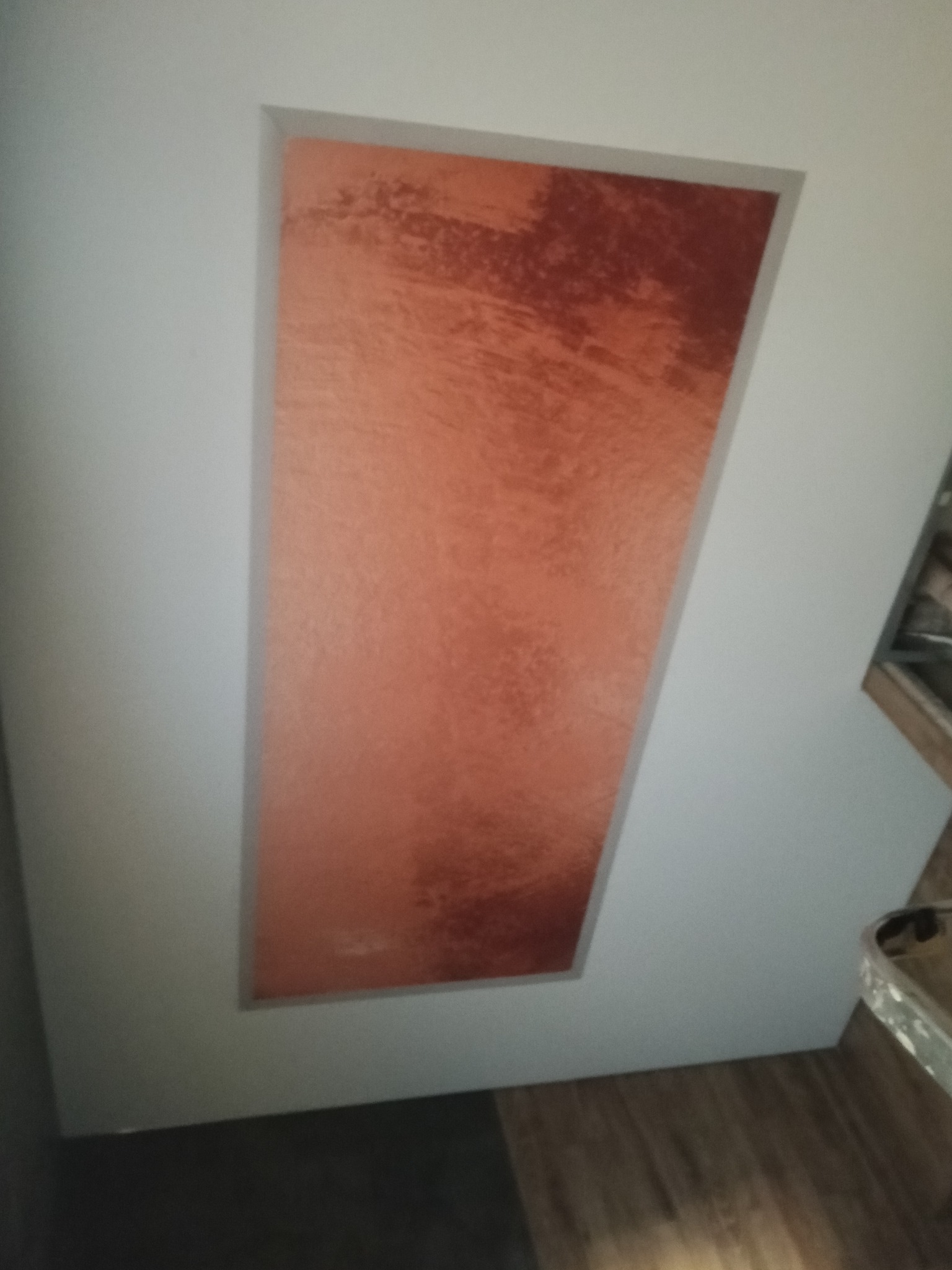 Błyszczący, miedziany sufit napinany z efektem ombre, wkomponowany w białą ramę. Widoczny fragment podłogi i ściany. Nietypowy kształt wnęki.