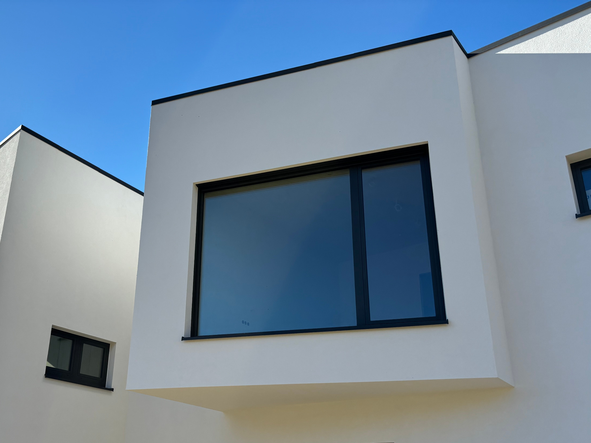 Nowoczesny budynek z białymi ścianami i czarnymi ramami okiennymi pod błękitnym niebem, minimalistyczna architektura.