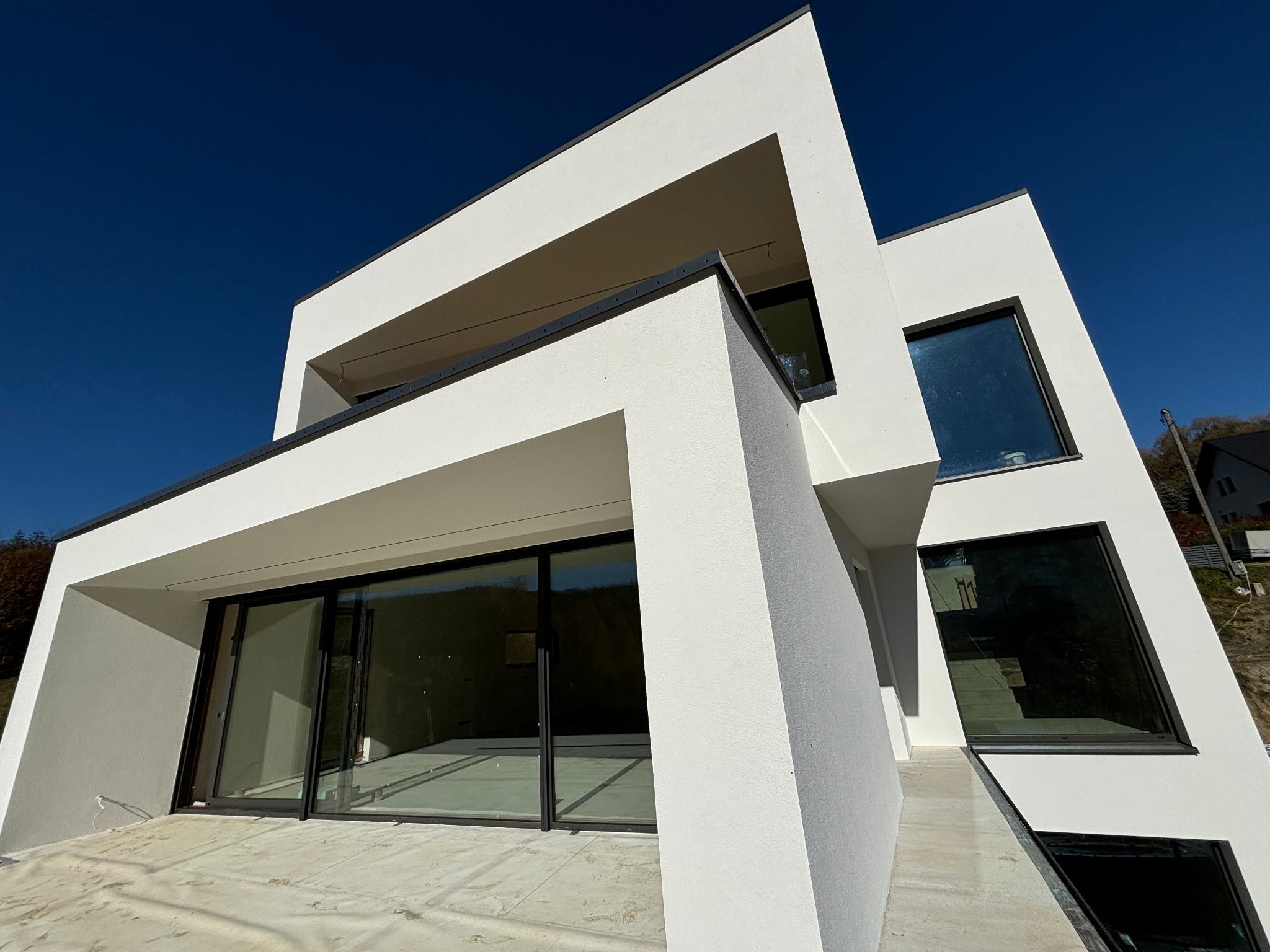 Nowoczesny, biały dom z płaskim dachem i dużymi oknami, widok z dołu w słoneczny dzień, elewacja o fakturze baranka.