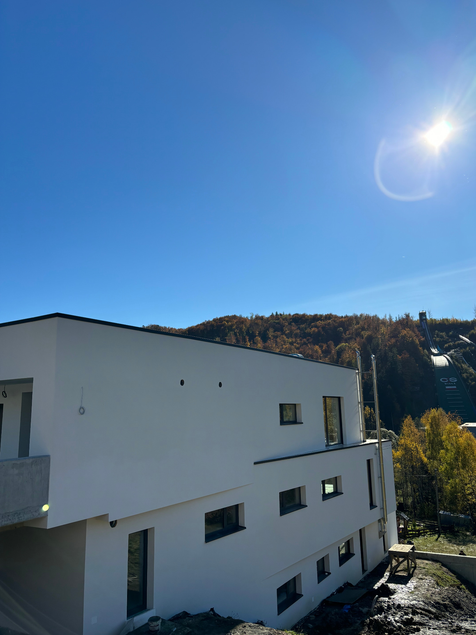 Nowoczesny, biały dom z płaskim dachem w słoneczny dzień, w tle skocznia narciarska w Wiśle Malince