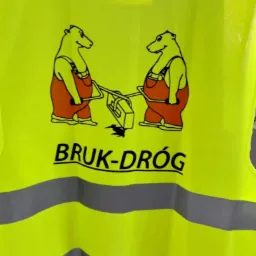 Żółta kamizelka odblaskowa z logo firmy 'BRUK-DRÓG' przedstawiającym dwa niedźwiedzie w kombinezonach obsługujące maszynę do układania kostki.
