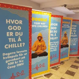 Rząd roll-upów reklamowych z nadrukiem grafiki przedstawiającej osobę w pozycji lotosu, z tekstem w języku skandynawskim i logo 'Doodle'.