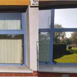 Okna budynku, jedno z szyb jest przyciemnione folią, widać odbicie otoczenia